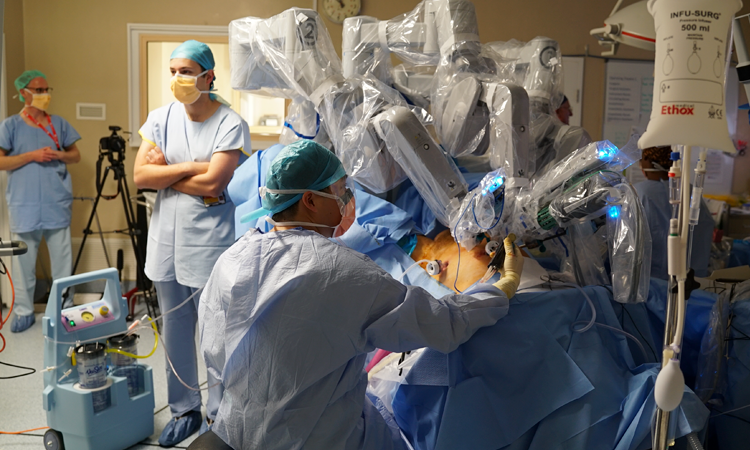 Team of surgeons wearing scrubs and masks around an operating table with plastic-covered machine over patient