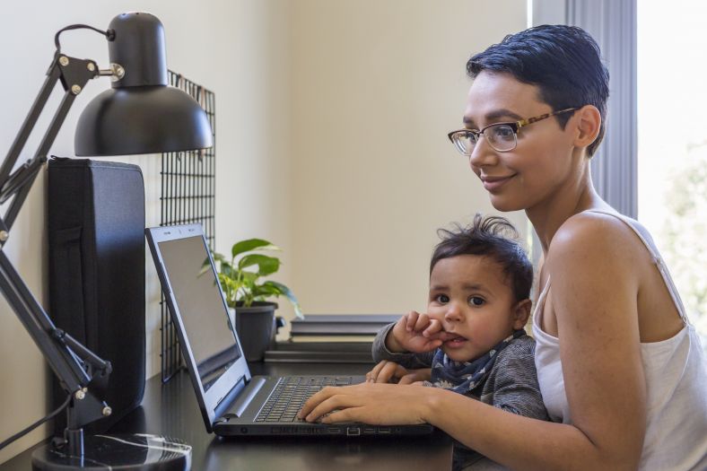 Aboriginal Mother with baby Son at the desk on her laptop. Mother is smiling and intrigued.