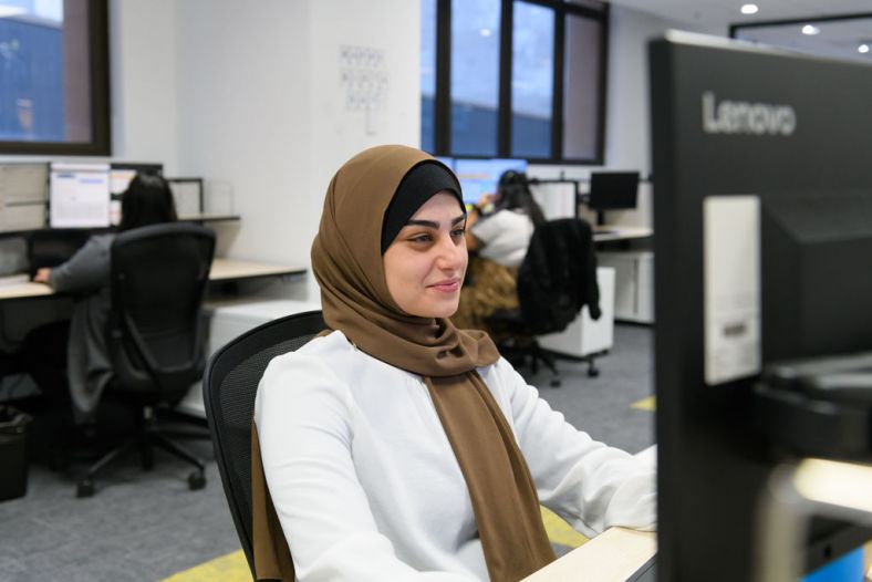 A woman is sitting looking happily at a computer in an office