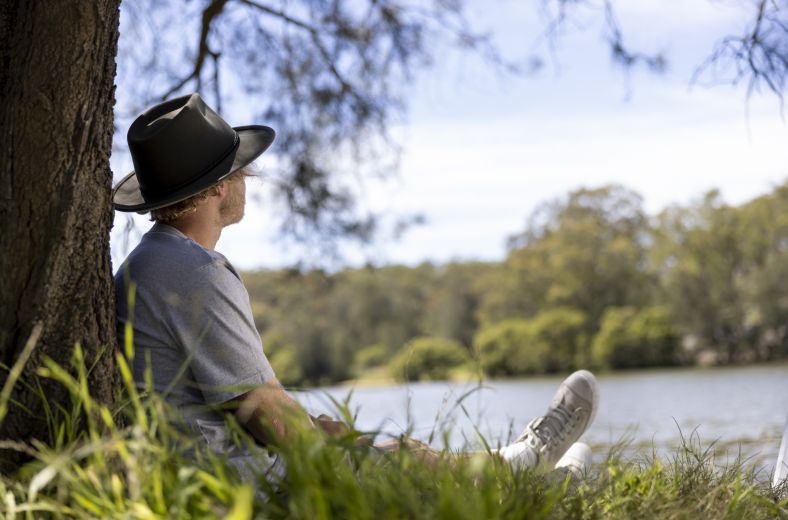 Man sitting under tree near river at Picnic Point