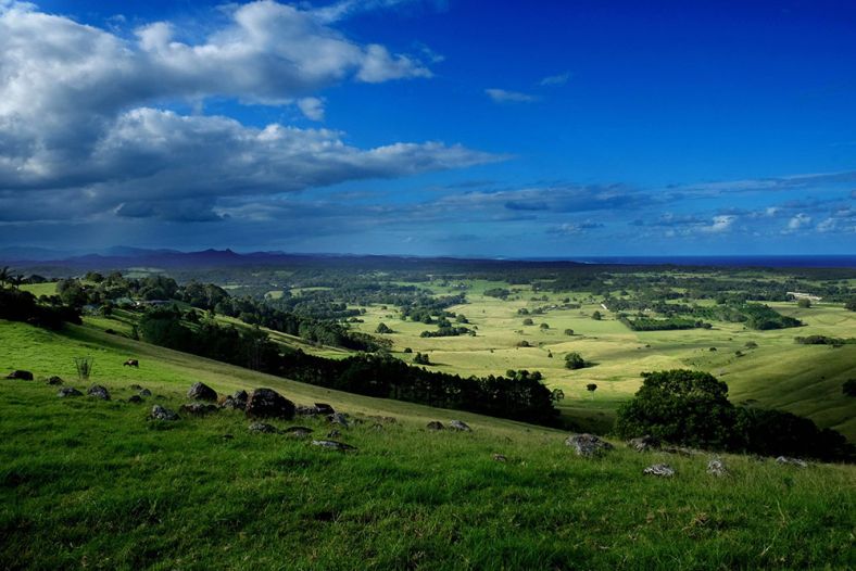 Overlooking a green lush valley with fields and trees. The sky is bright blue with some clouds to the left