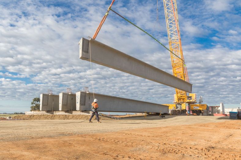 Workperson checks large concrete blocks being moved by giant crane