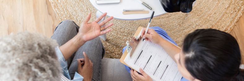 Nurse looking sitting on couch talking to person while looking and papers