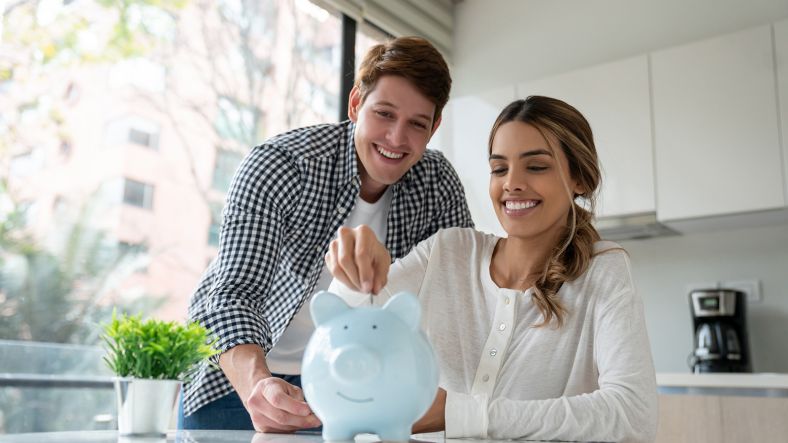 Young couple smiling and putting coins into blue piggybank