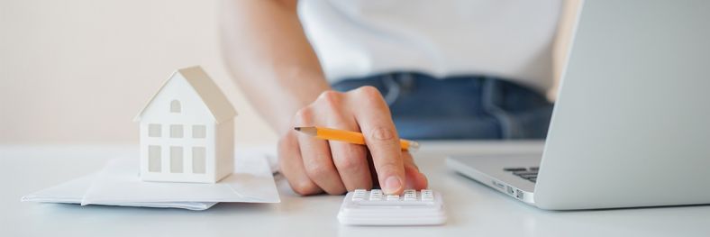 Person typing on a calculator with a tiny model house next to them