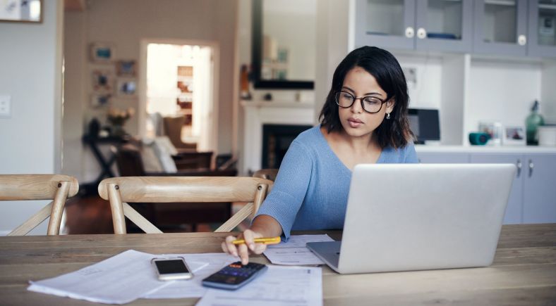 Young woman using laptop and calculator