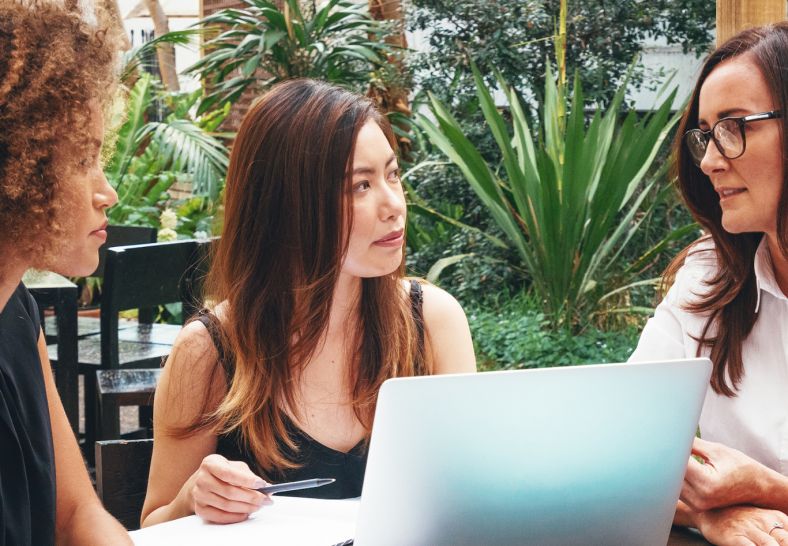 Three woman sitting at a desk with a laptop discussing their strata plan.