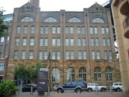 Multi-storey heritage brown brick building with crescent windows near roof.