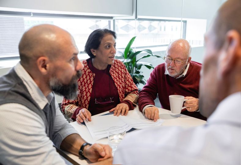 Three men and one woman sitting around a table with papers discussing their strata committee