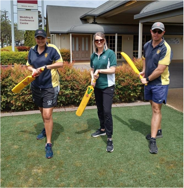 Image L to R: Kate Menz- Murrumburrah Public, Corina Gardiner- Wombat Public, and Brendon Shean - Murrumburrah Public at the 2022 PACE training program. They are standing on a lawn outside a conference centre. They are holding cricket bats and holding a batting pose.