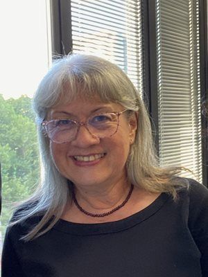 Image of Dr Barbara Taylor, Director of Research at MLHD. She has grey and silver long hair and is wearing glasses and a black top and smiling.