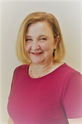 Griffith Hospital General Manager, Joanne Garlick is standing against the plain background and is smiling and facing forward.