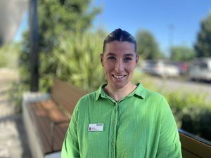 Image of Rachael Murdoch an allied health assistant in Wagga. She looking straight at the camera. She is wearing a green shirt and standing against a natural background of trees and the sky.