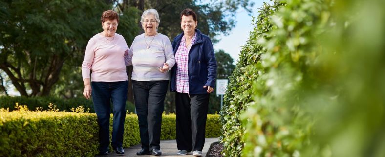 Three older women smiling and walking in a park.