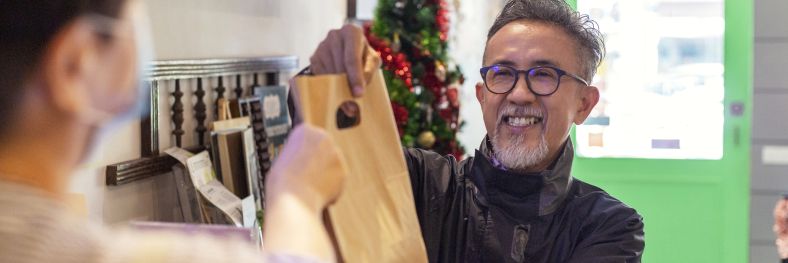 A man delivers a food order to a woman in a shop.