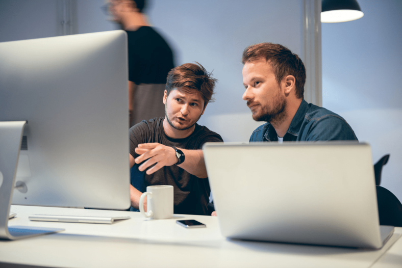 Two people discussing while sitting at computer and laptop