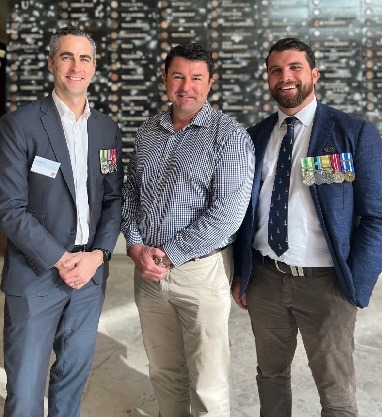 Image of three men dressed in suits smiling at camera wearing veterans or emergency services medals 