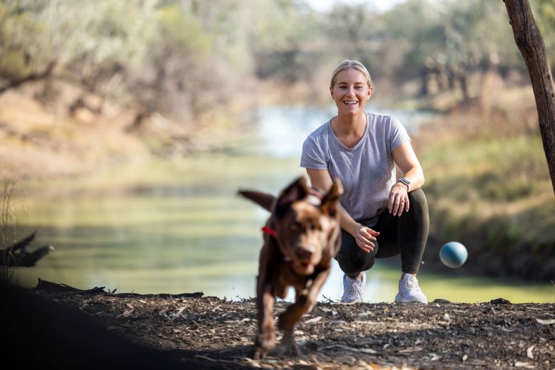 A woman and her dog playing fetch by the river