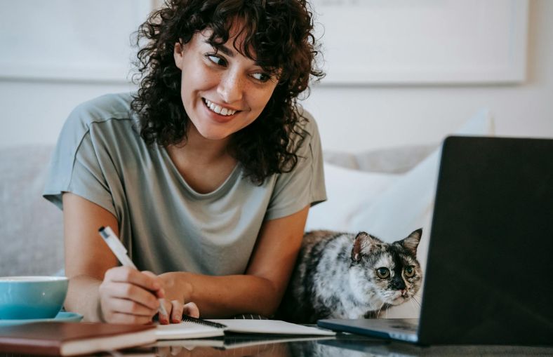 A person sat at a desk with a laptop and a notebook.