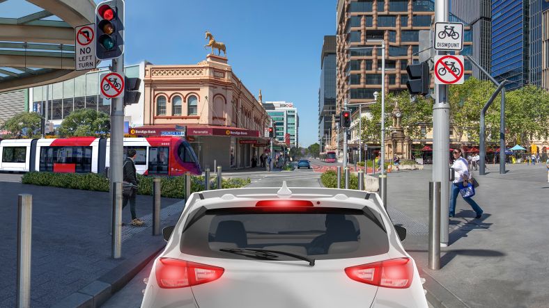 A white car is seen in the centre of the image with a heritage building at the top left and new apartment block at the top right of the image.