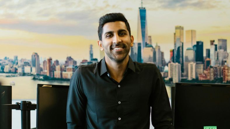 A man leading against a desk in an office with the graphic of a city in the background.