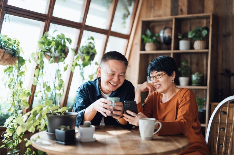 Couple sitting at table doing online shopping together on a mobile phone.