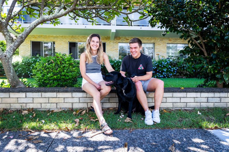 Two young adults with a dog outside apartments