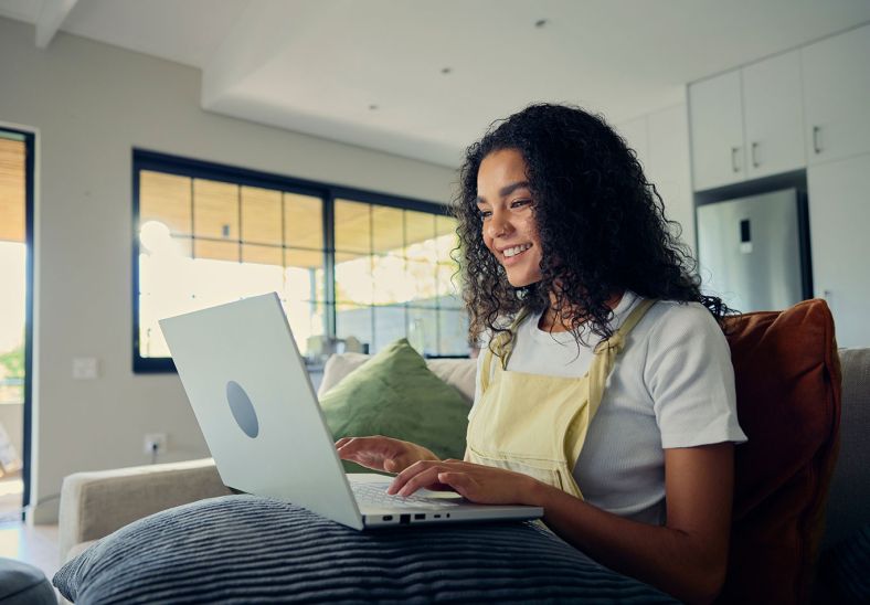 A woman smiling while using her laptop and sitting on the couch