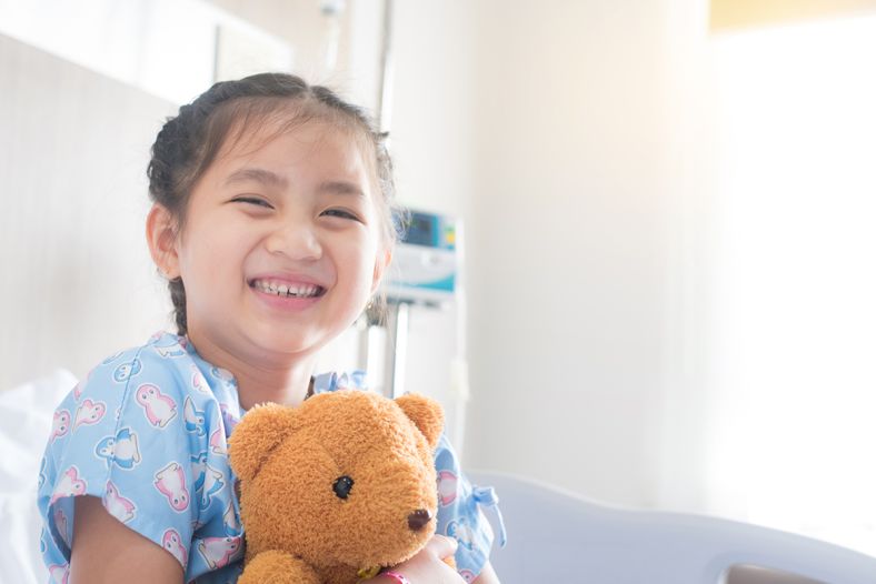 A child in hospital smiling and holding a teddy bear