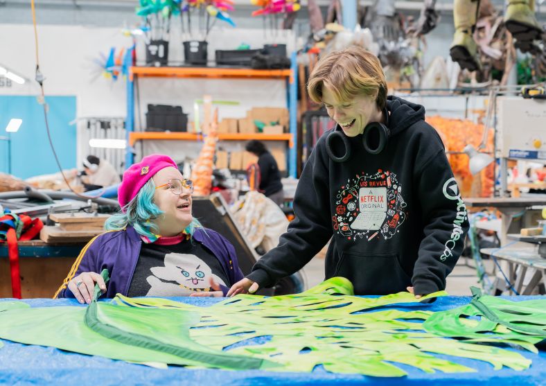 Two artist practitioners with disability smiling as they work together on a visual art installation in a workshop