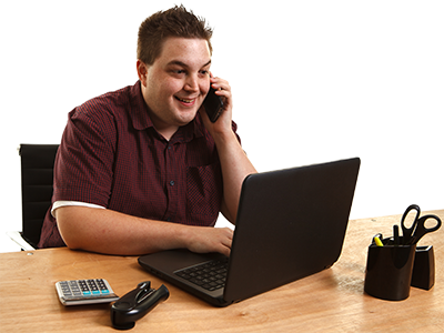 A person sitting in front of a laptop takling on the phone. 