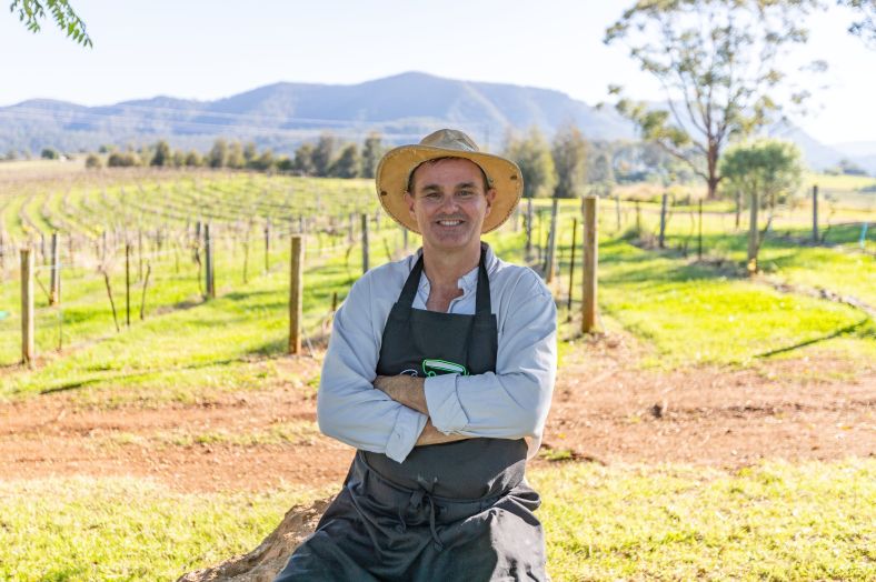 A tour guide smiling at the camera in front of a scenic Hunter Valley field