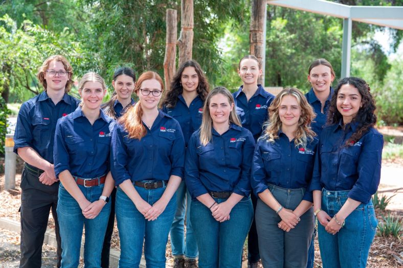 group of graduates smiling at the camera with a lush bushland background