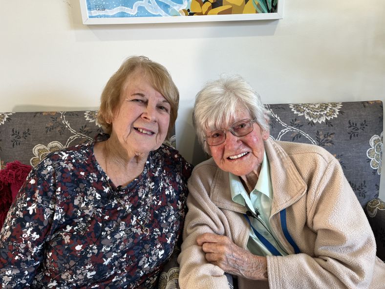 Val and Kathy, NSW proud grandparents, in a nursing home sitting side by side in chairs.