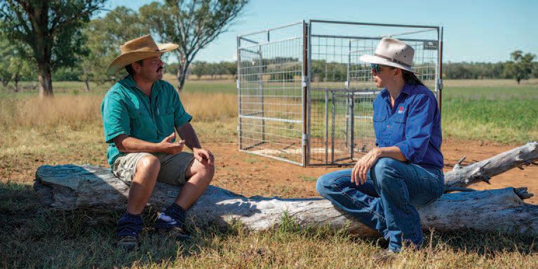 landholder and LLS staff member sitting on a log in front of a metal pest animal trap