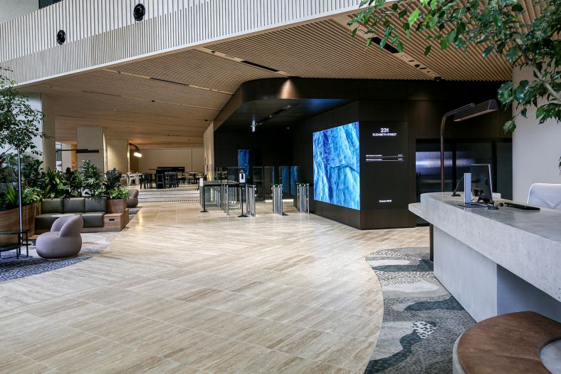 Foyer in office with lounge chairs, tables, barrier entry to lifts by swipe card and reception desk.