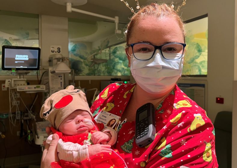 A nurse holding a baby in hospital wearing Christmas clothes