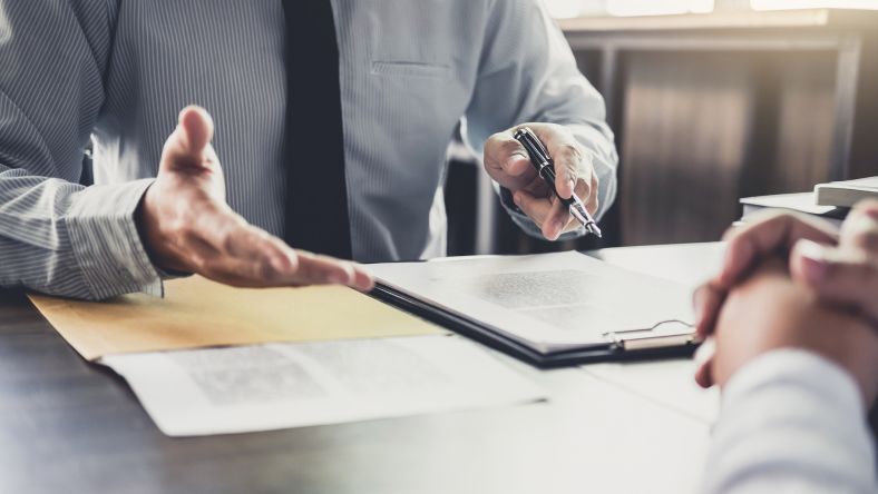 two people sitting at a desk with the focus on their hands as they go through a mediation process