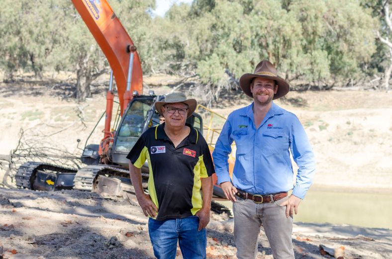 Local Land Services staff stand in front of an excavator that is placing stands in the Murray river.