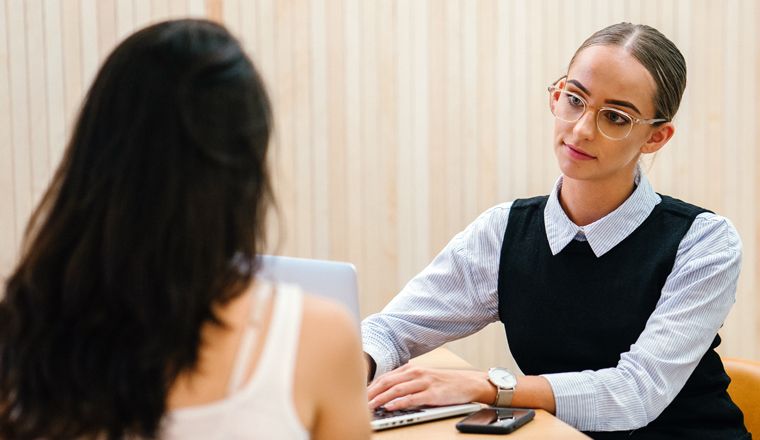 A lawyer is sitting with a client at a table in a meeting room and is interviewing her