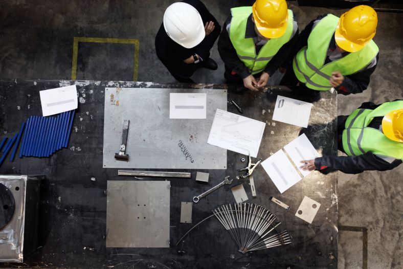 Workers and manager in safety helmets working with documents at factory