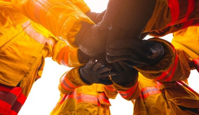 A group of firefighters in a circle, touching hands.