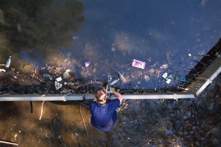 A person installs a camera over a waterway for the Smarter, Cleaner Sydney Harbour project.