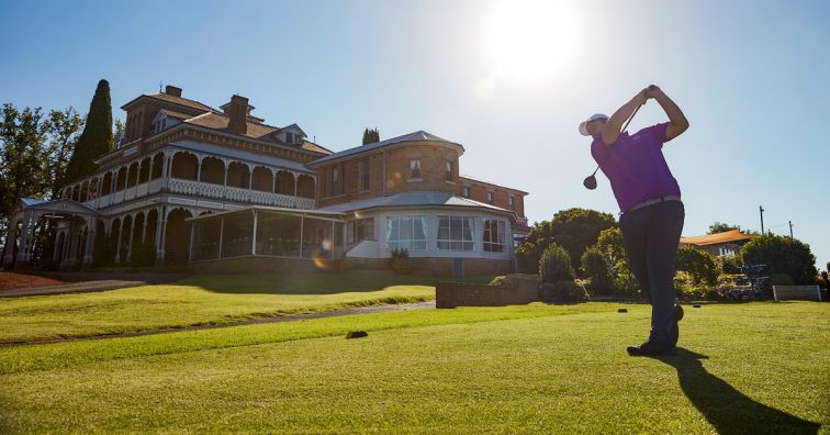 man playing golf on the greens at Duntry League with heritage clubhouse in the background