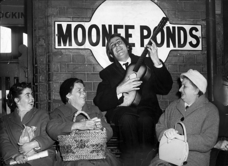 Barry Humphries pictured in 1962 with a captive audience as he sings the Moonee Ponds Serenade at Moonee Ponds train station.