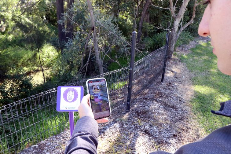 A person scans a QR code using their smartphone camera to open the Muscle Creek Augmented Reality Tour platform.