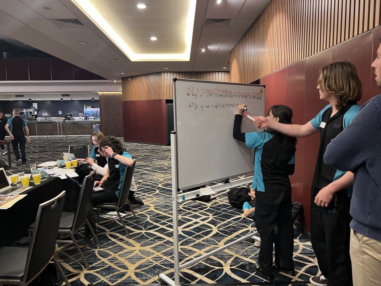 Students writing on the whiteboard with teacher watching 