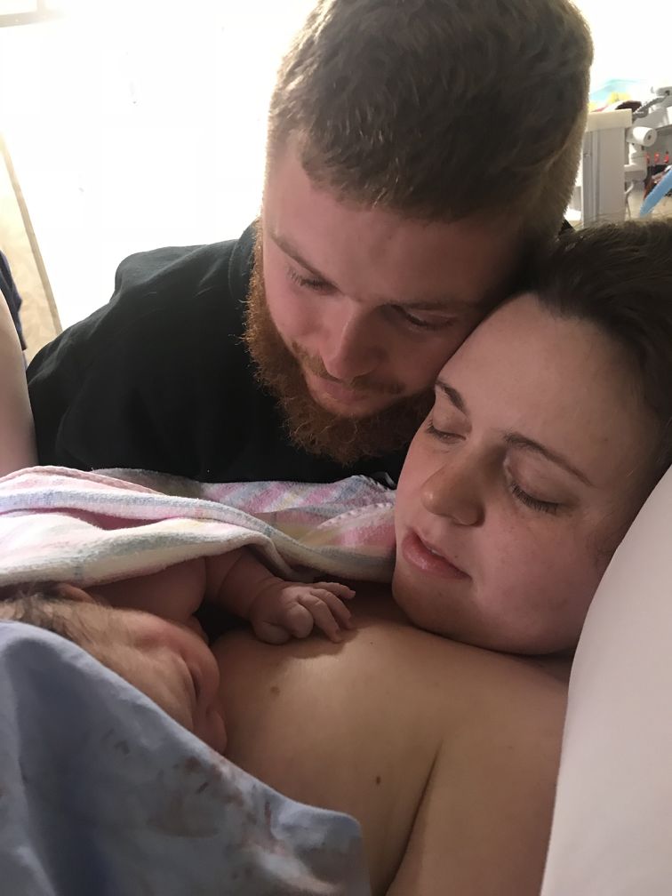 Woman breastfeeding baby in hospital bed with partner