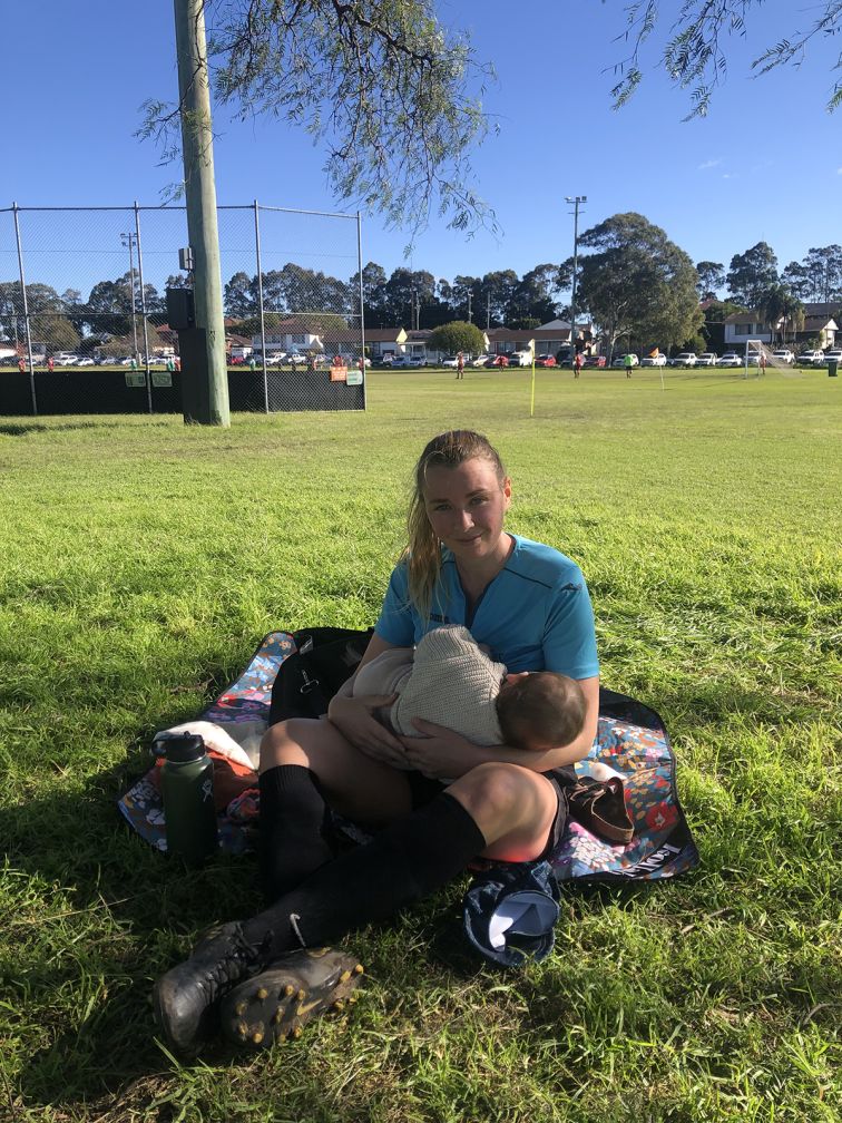 Woman breastfeeding baby at a sporting field