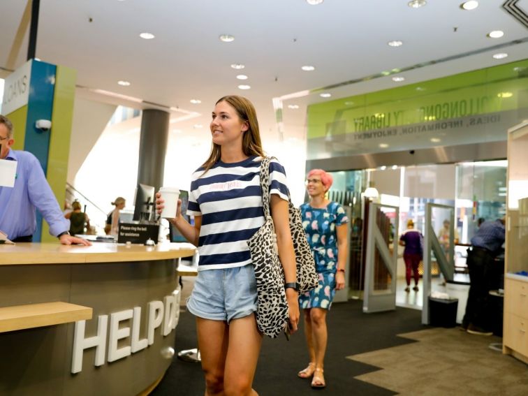 A young woman holding a coffee enters the library